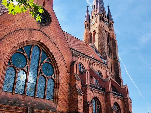 Außenansicht der Apostelkirche mit markantem Kirchturm und Backsteinfassade bei blauem Himmel