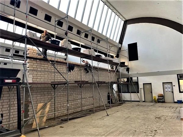Bauarbeiten bei Conti: Handwerker auf einem Gerüst in einer Industriehalle mit Backsteinmauer
