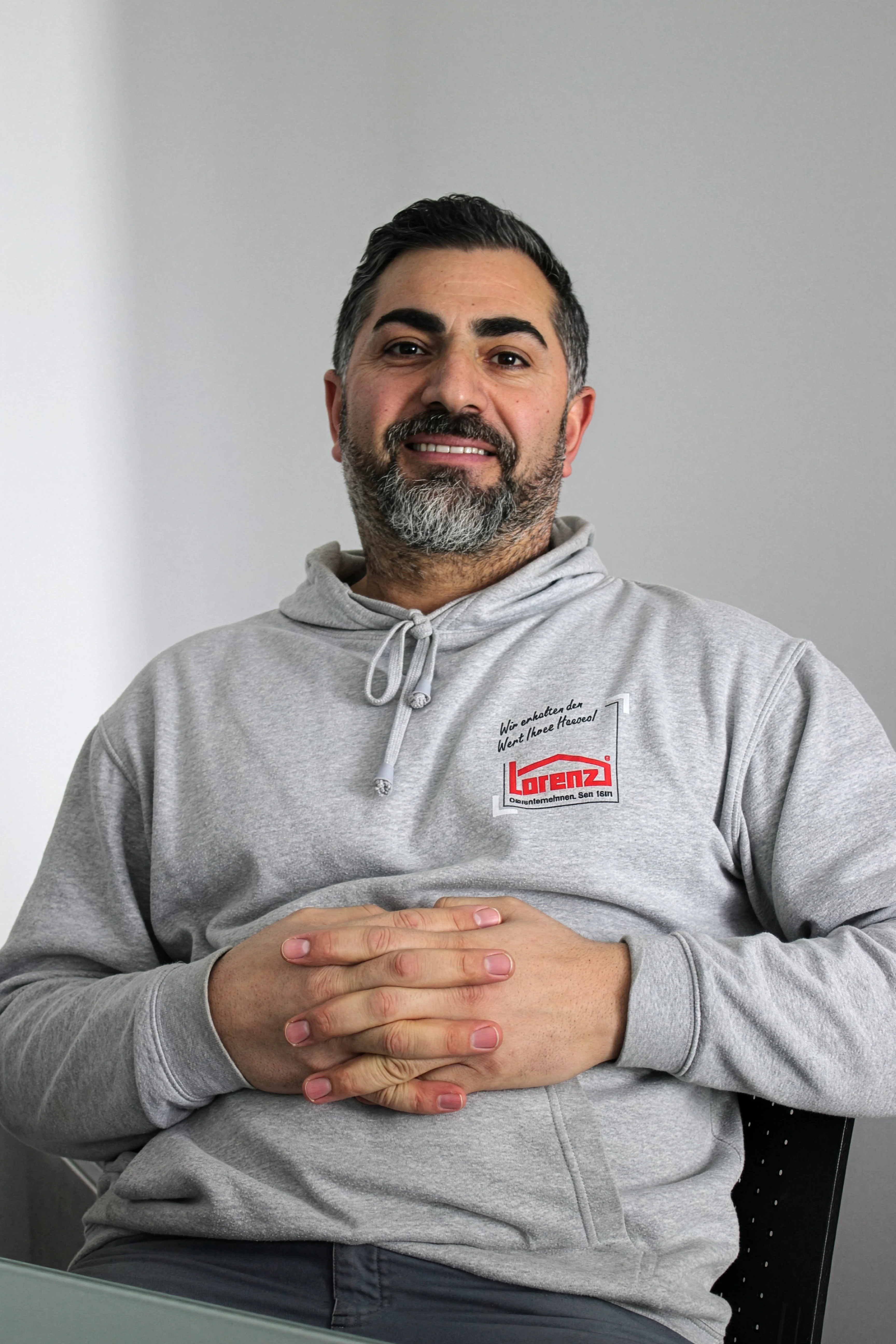Mikael Bilek mit grauem Lorenz Pullover, sitzt mit verschränkten Händen