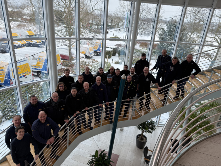 Gruppenfoto von Mitarbeitern auf einer Treppe in einem modernen Firmengebäude mit Blick auf verschneite Fahrzeuge draußen