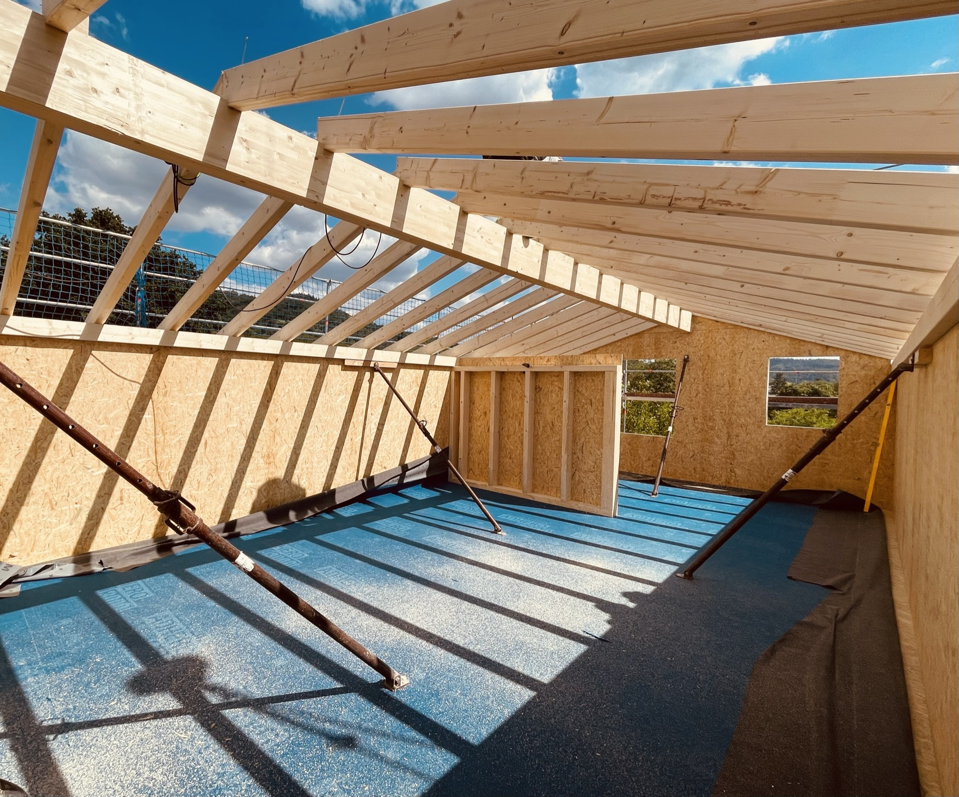 Dachstuhl aus Holz im Rohbau mit OSB-Platten und blauer Baufolie, Baustelle bei sonnigem Wetter