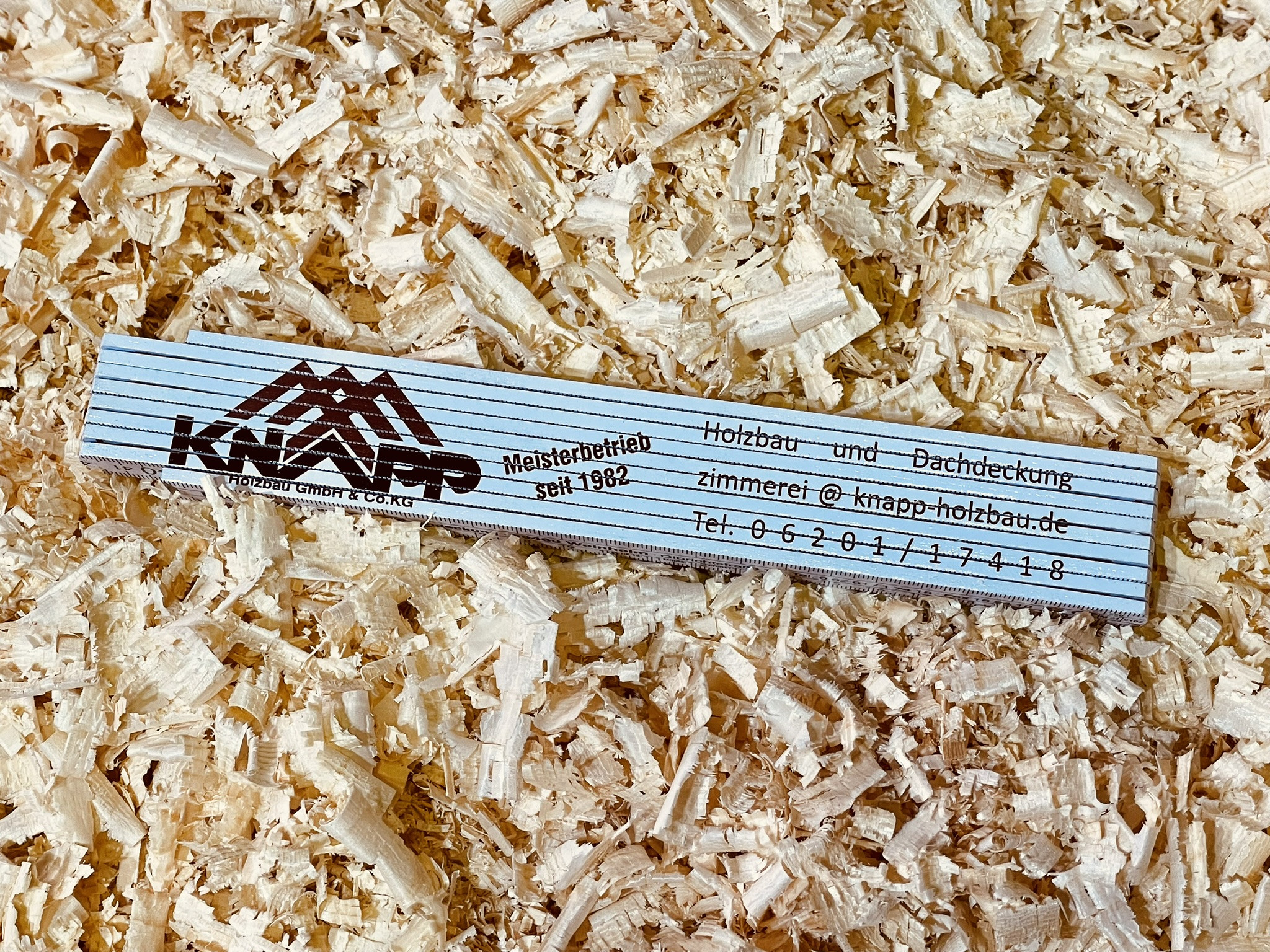 Zollstock der Knapp Holzbau GmbH & Co. KG auf Holzspänen, Meisterbetrieb für Holzbau und Dachdeckung seit 1982