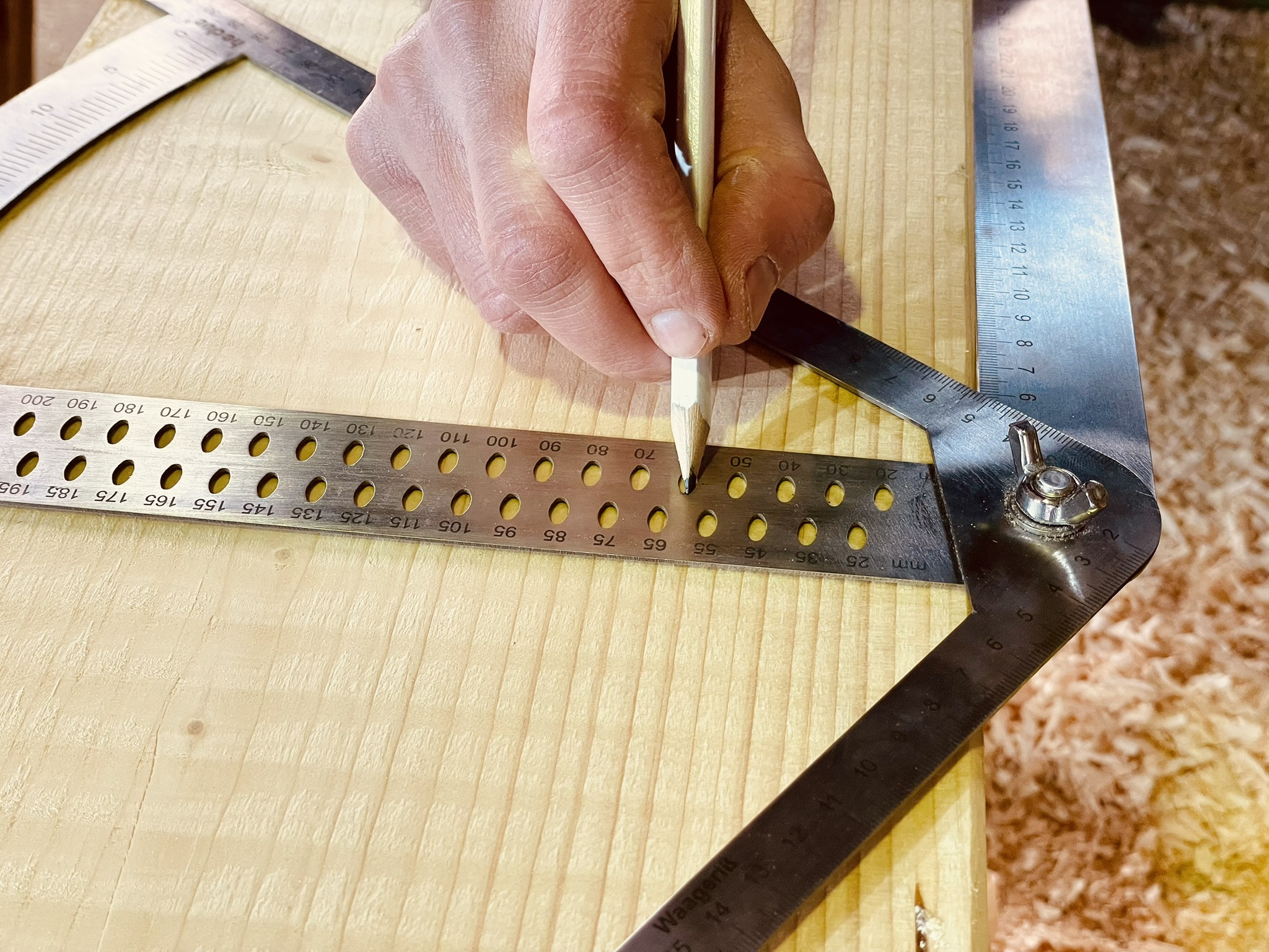 Hand zeichnet mit Bleistift und Metallwinkel eine Markierung auf Holz, Nahaufnahme beim Tischlern