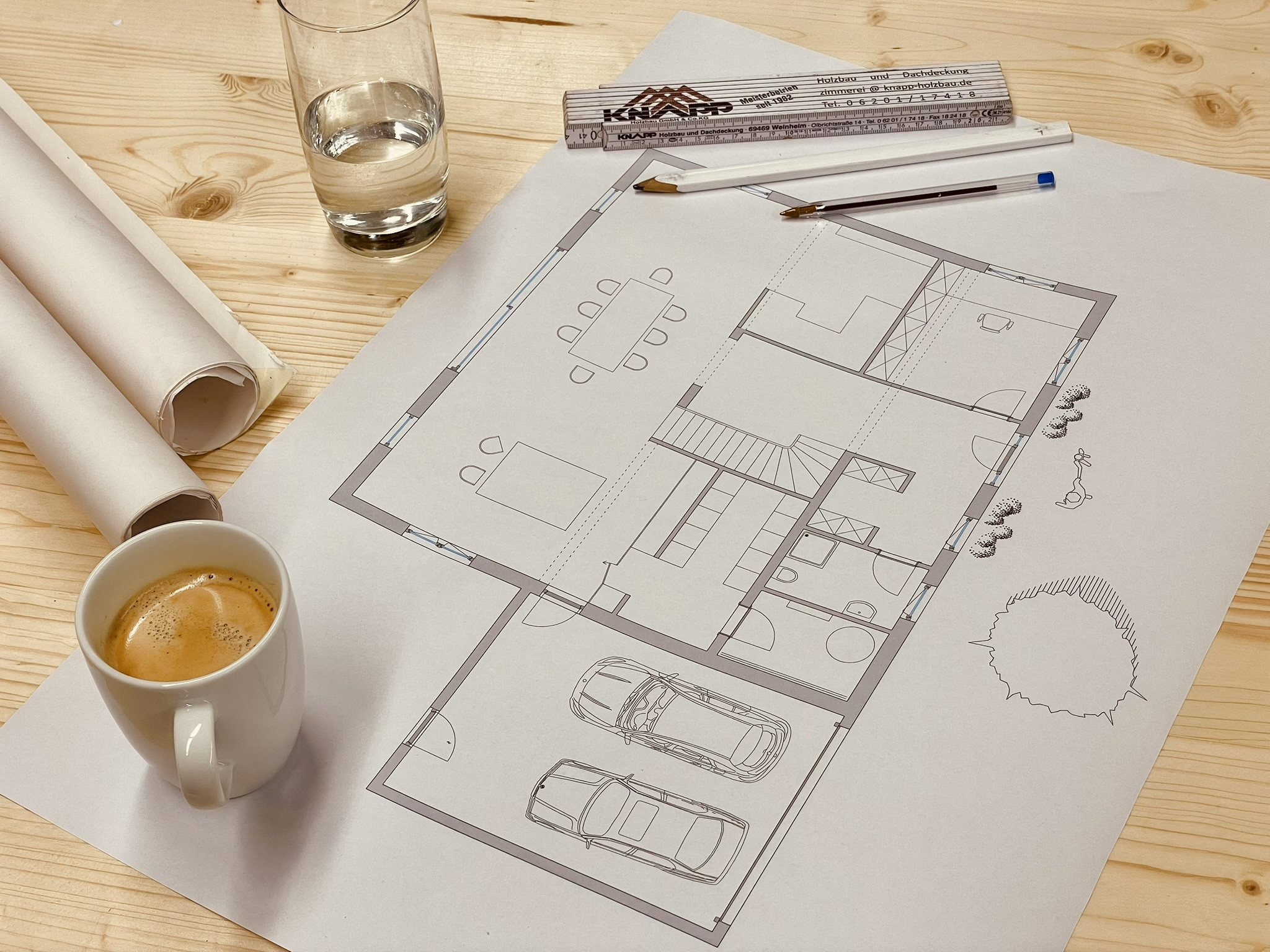 Architektenzeichnung eines modernen Einfamilienhauses mit Grundriss, Lineal, Stift und Kaffeetasse auf Holztisch