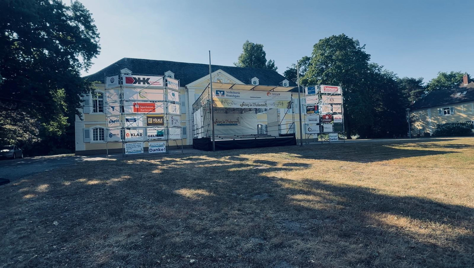 Bühne mit Sponsorenbanner vor historischem Gebäude, Volksbank Kraichgau und Sparkasse Karlsruhe als Sponsoren beim Event Swing'n'Kultur 2025.