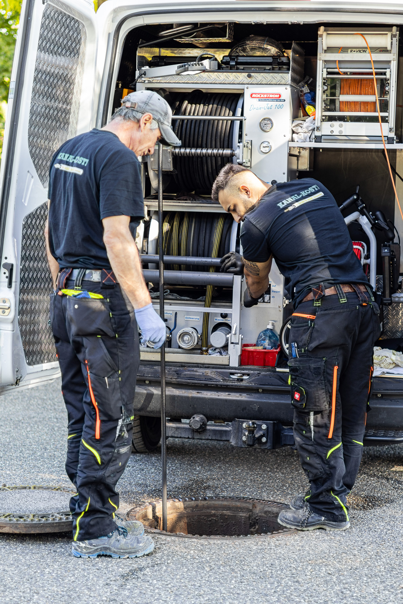 Arbeiter führen professionelle Kanalreinigung mit Spezialfahrzeug durch Zwei Arbeiter bei der Kanalreinigung mit Spezialfahrzeug und Ausrüstung
