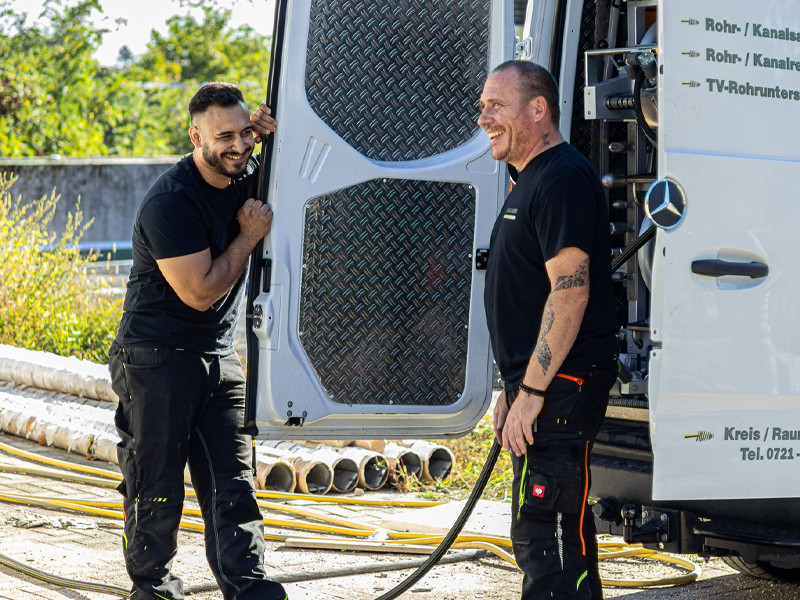 Handwerker bei der Arbeit an einem Mercedes-Benz Transporter auf einer Baustelle Zwei Handwerker arbeiten an einem Mercedes-Benz Transporter auf einer Baustelle