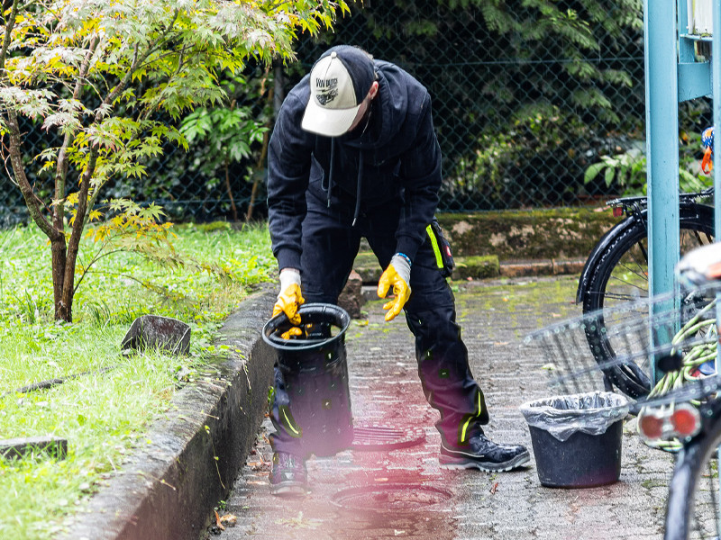 Reinigung eines Außenbereichs durch eine Person mit Eimer und Handschuhen Person mit gelben Handschuhen reinigt einen Außenbereich mit Eimer und Müllbeutel