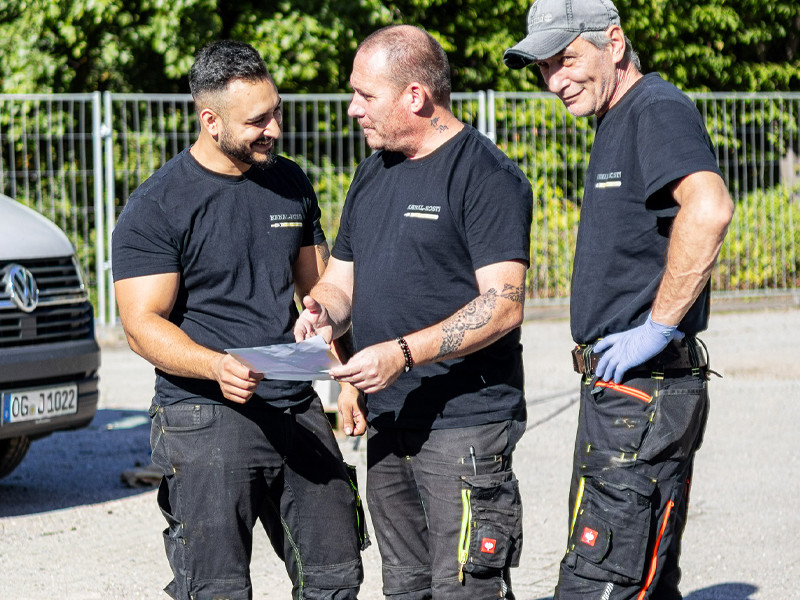 Handwerker im Austausch auf einer Baustelle mit Arbeitskleidung und Dokumenten Drei Handwerker im Gespräch auf einer Baustelle, tragen Arbeitskleidung und besprechen Unterlagen