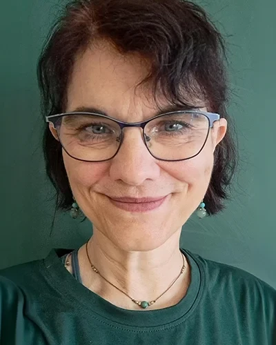 Porträt von Magda Zetka mit Brille vor grünem Hintergrund