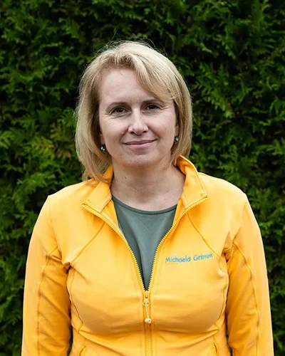 Porträt von Michaela Grimm mit gelber Jacke vor grünem Hintergrund