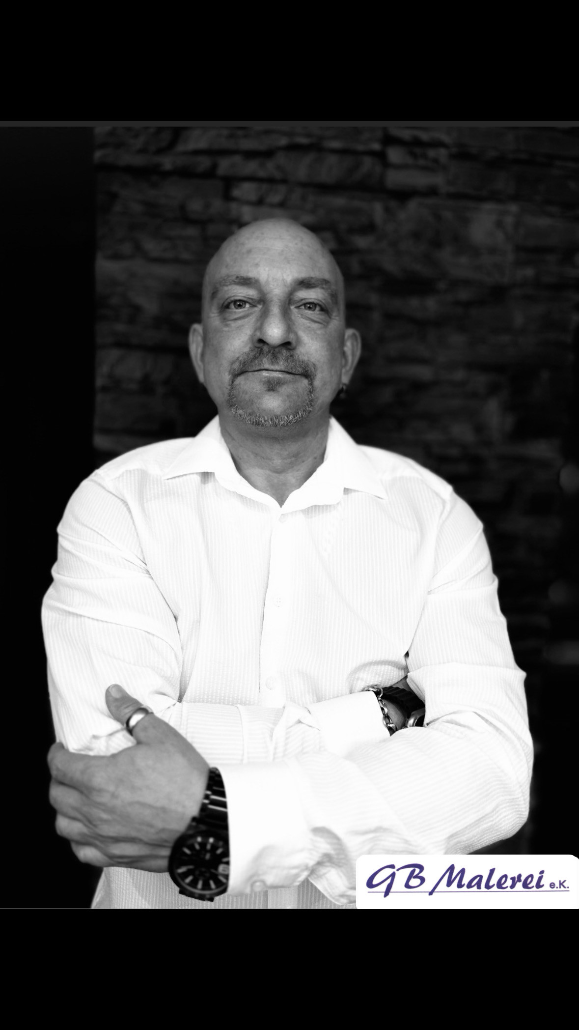 Mann mit weißem Hemd und verschränkten Armen vor dunklem Hintergrund