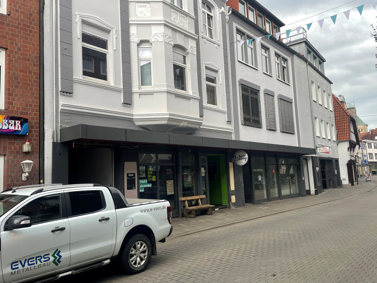 Straßenszene mit Geschäftsgebäude und geparktem weißen Pickup in einer deutschen Innenstadt, aufgenommen am 28.08.2025