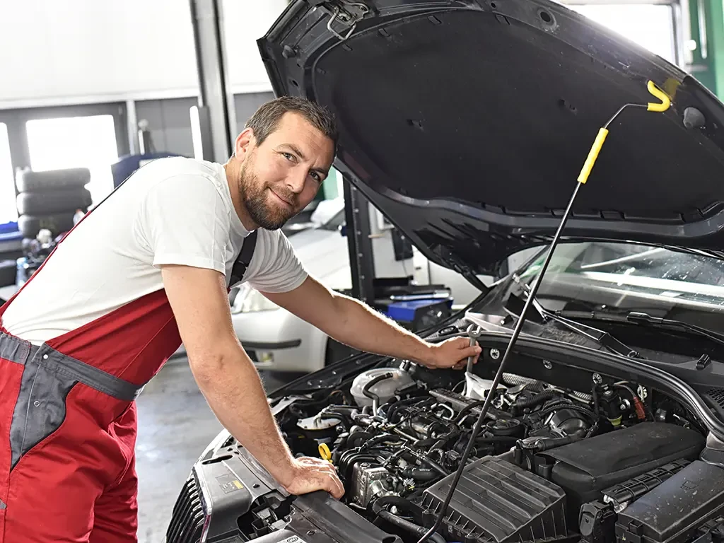 Automechaniker arbeitet in einer Werkstatt am offenen Motor eines Autos