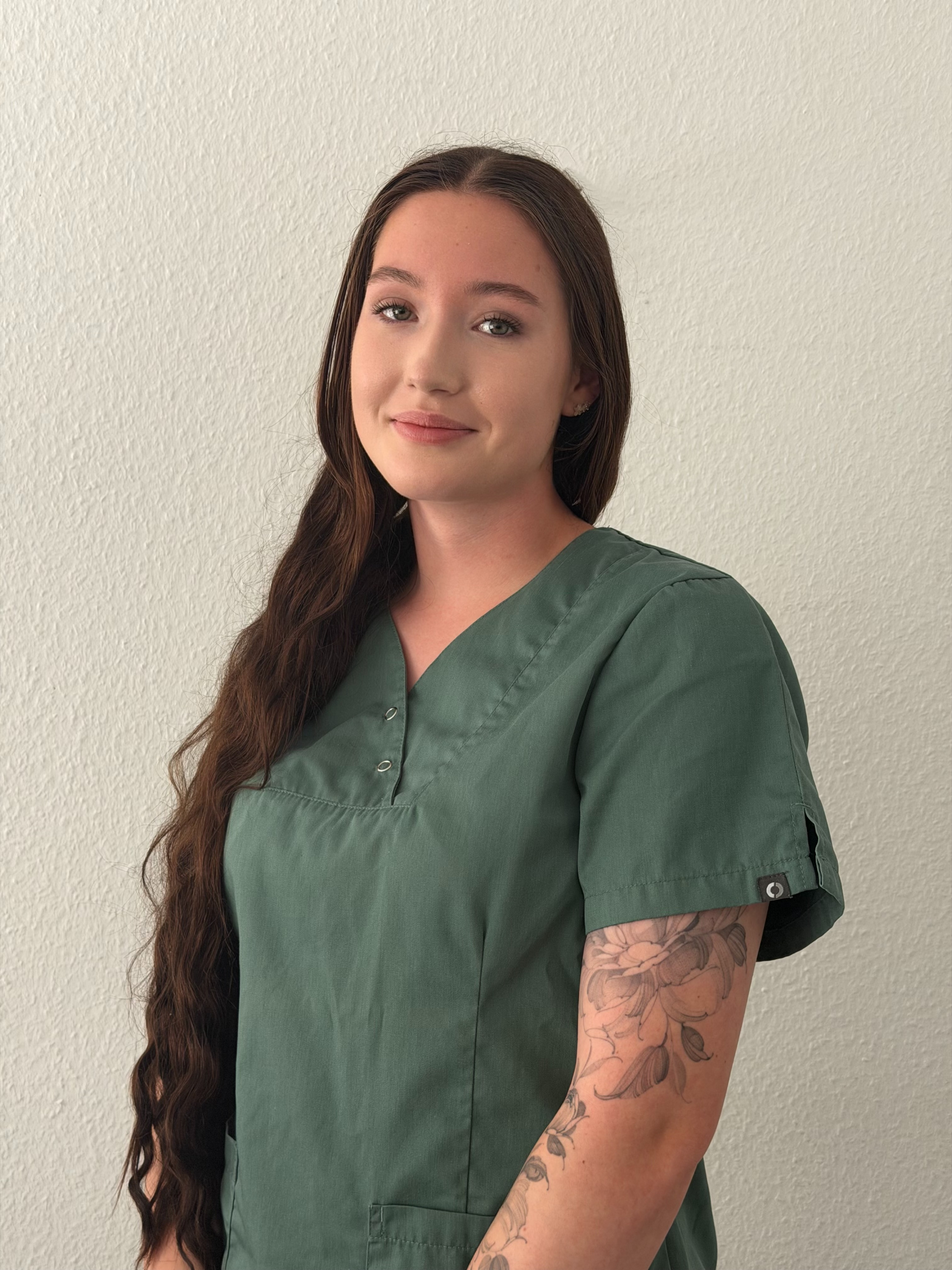 Porträt einer jungen Frau mit langen braunen Haaren und grünem Oberteil, die vor einer hellen Wand steht. Der Dateiname 'linea' wird berücksichtigt.