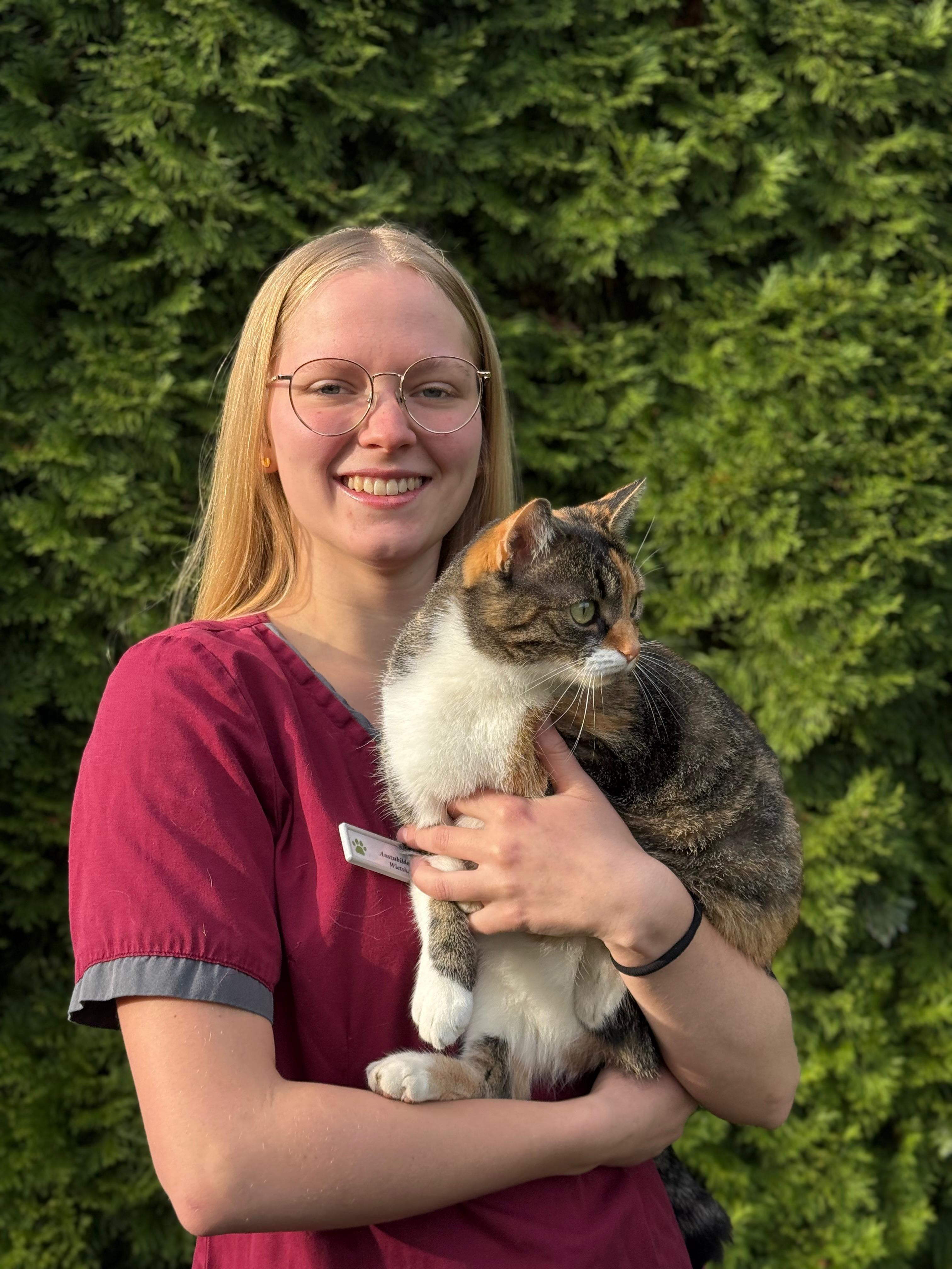 Tierarzthelferin hält eine Katze im Freien vor grüner Hecke