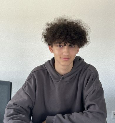 Yassin am 06.08.2025 mit dunklem Hoodie Yassin sitzt mit dunklem Hoodie an einem Tisch vor einer hellen Wand
