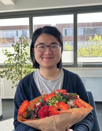 zc aktuelles: Person mit Blumenstrauß im Büro vor Fenster