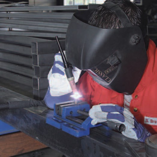 Schweißer bei der Arbeit mit Schutzmaske und Handschuhen in einer Werkstatt