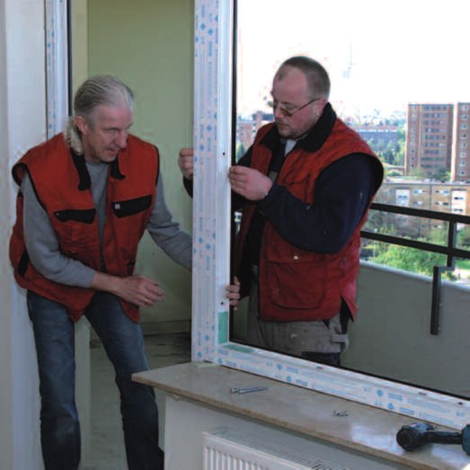 Zwei Handwerker beim Einbau eines Fensters auf einem Balkon in einem Mehrfamilienhaus