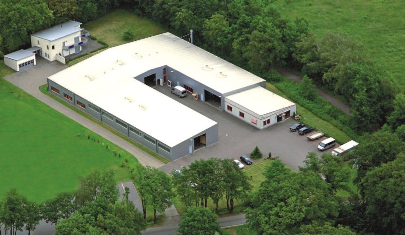 Luftaufnahme eines Gewerbegeländes mit Halle und Bürogebäude im Grünen