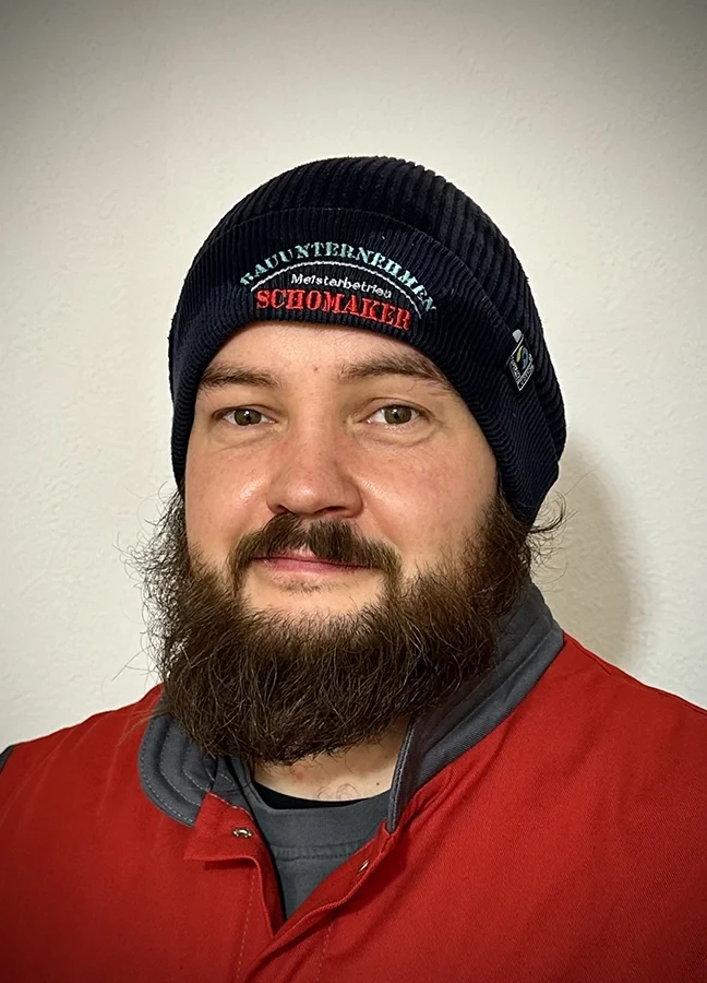 Peter Nadolny mit Mütze und roter Jacke vor hellem Hintergrund