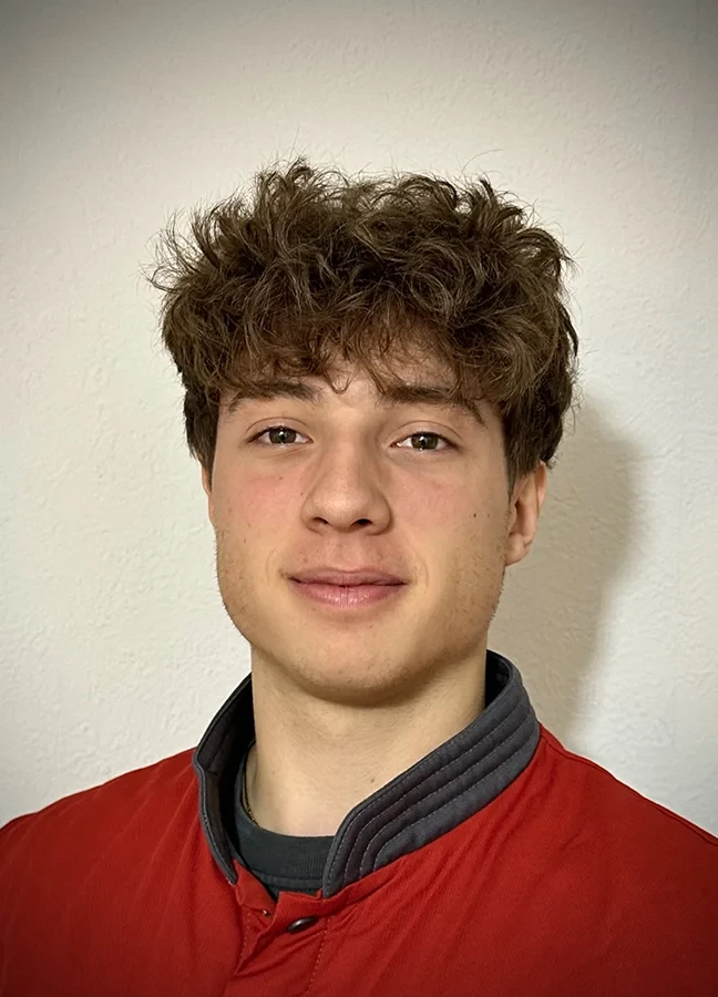 Louis Schomaker mit lockigen Haaren und roter Jacke vor einer weißen Wand