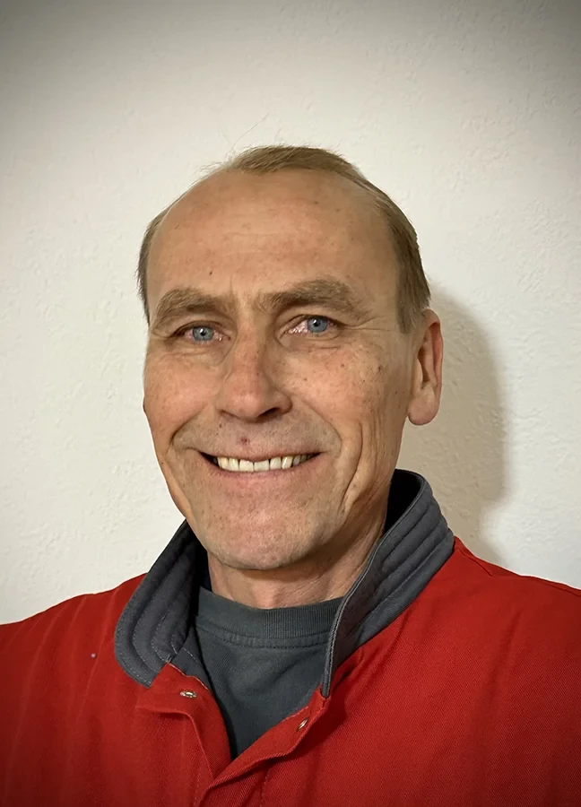 Aleksander Kusnekow in roter Jacke vor heller Wand