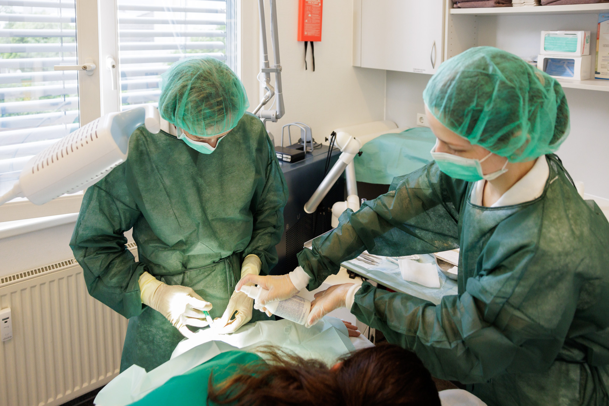 Ärzteteam bei einer Behandlung in einer modernen Arztpraxis, medizinisches Personal mit Schutzkleidung