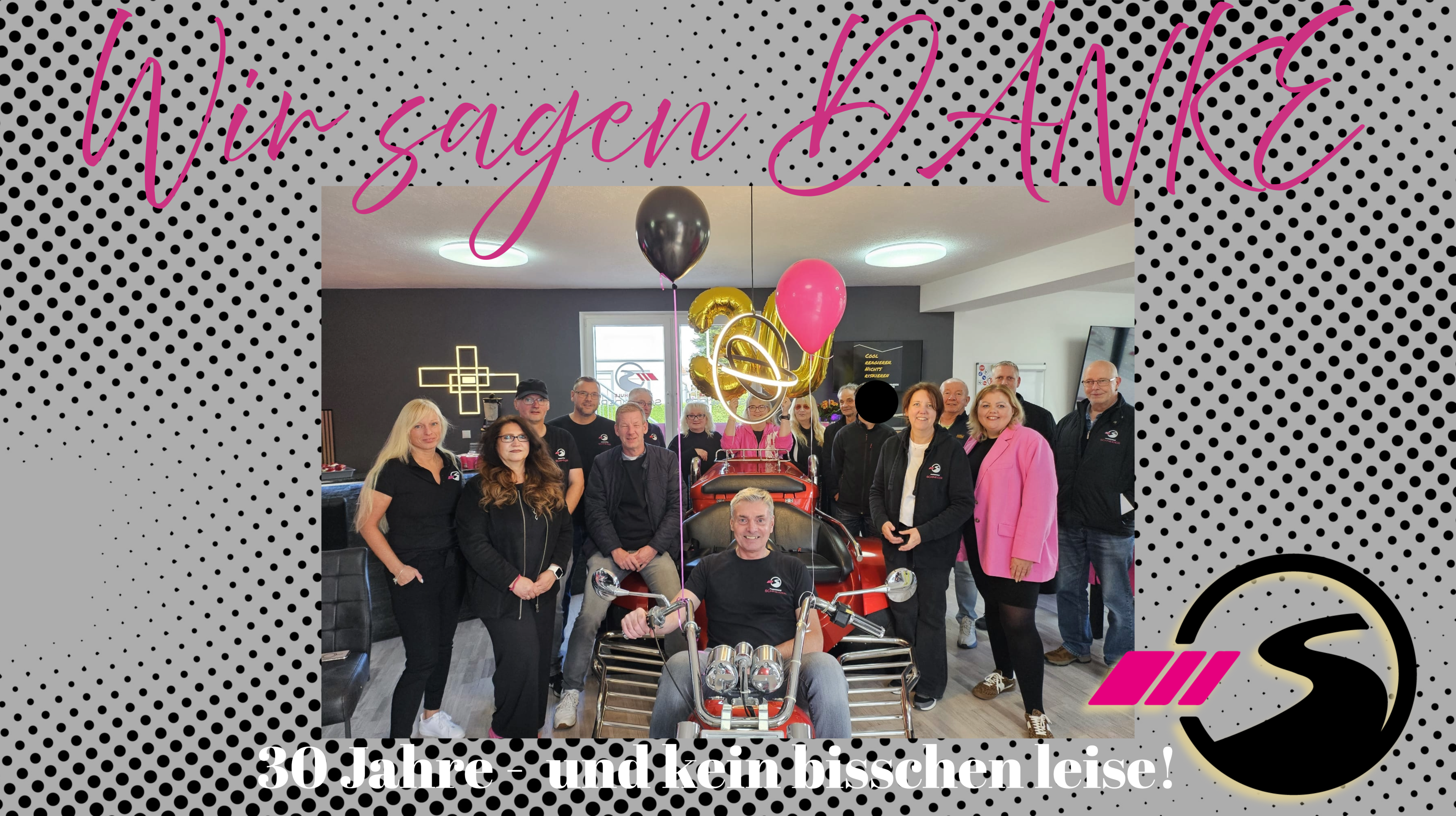 Gruppenfoto eines Teams bei einer Jubiläumsfeier mit Dekoration, Ballons und einem roten Trike im Vordergrund