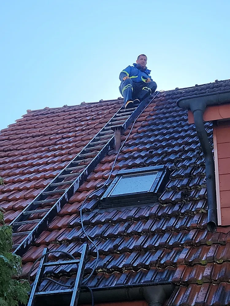 Dachdecker Gashi bei der Arbeit auf einem Ziegeldach mit Leiter und Dachfenster