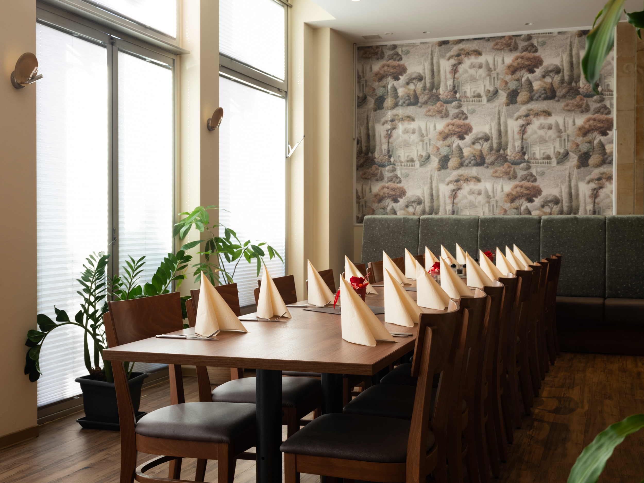 Modern eingerichtetes Restaurant mit langer Tafel, Holzmöbeln und gefalteten Servietten, bereit für Gäste