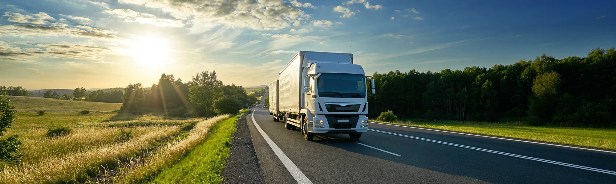 Moderner LKW auf Landstraße bei Sonnenuntergang – Headerbild für Startseite