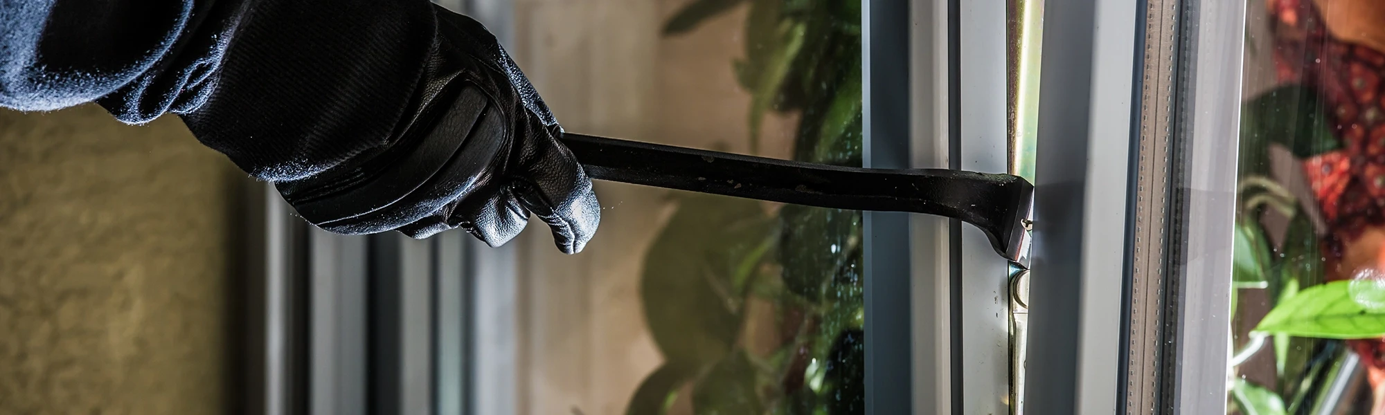 Nahaufnahme einer Hand mit Handschuh und Brecheisen an einem Fenster