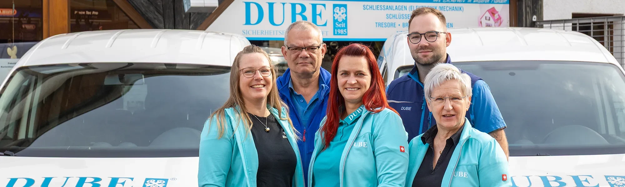 Teamfoto der Sicherheitsfirma DUBE auf der Startseite, drei freundliche Mitarbeiter vor dem Firmengebäude