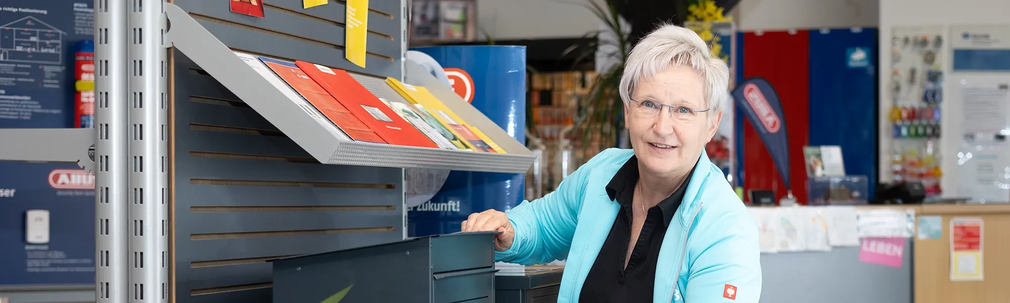 Freundliche ältere Frau an einem Arbeitsplatz mit Prospekten – Symbolbild für Jobs und Karriere