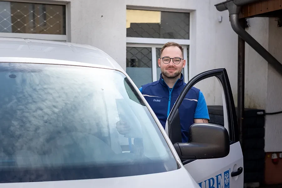 Mitarbeiter von DUBE steht an gefnetem Fahrzeug vor Firmengebe4ude