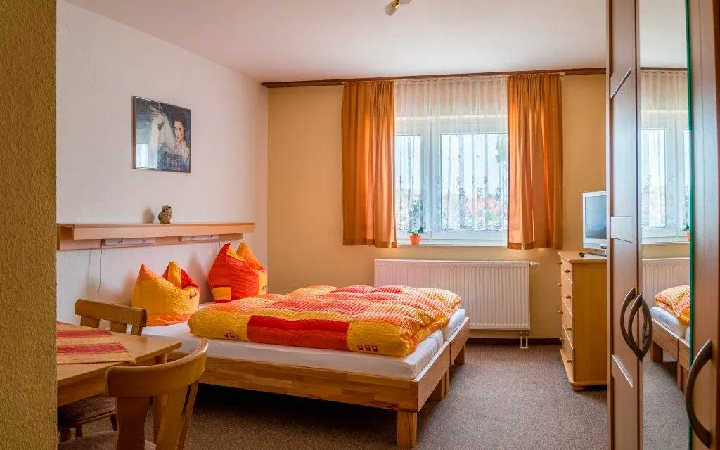 Gemütliches Zimmer in einer Pension mit Doppelbett, Fenster mit Vorhängen und Holzmöbeln