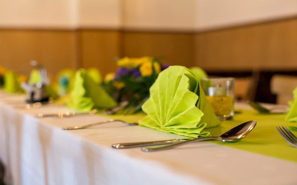 Festlich gedeckter Tisch in einer Pension mit grün gefalteter Serviette und Blumendekoration