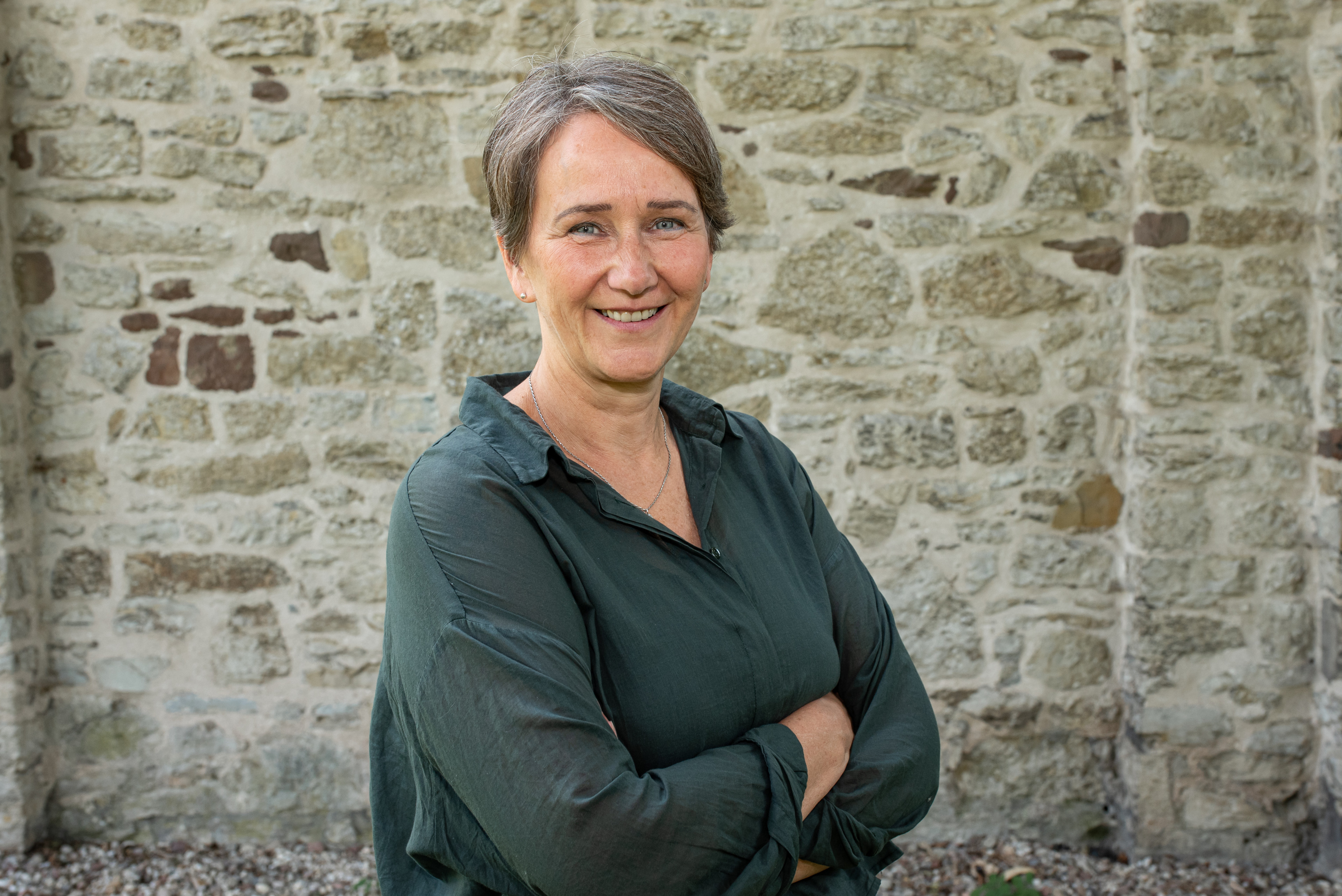 Frau mit dunkler Bluse steht vor einer Steinmauer