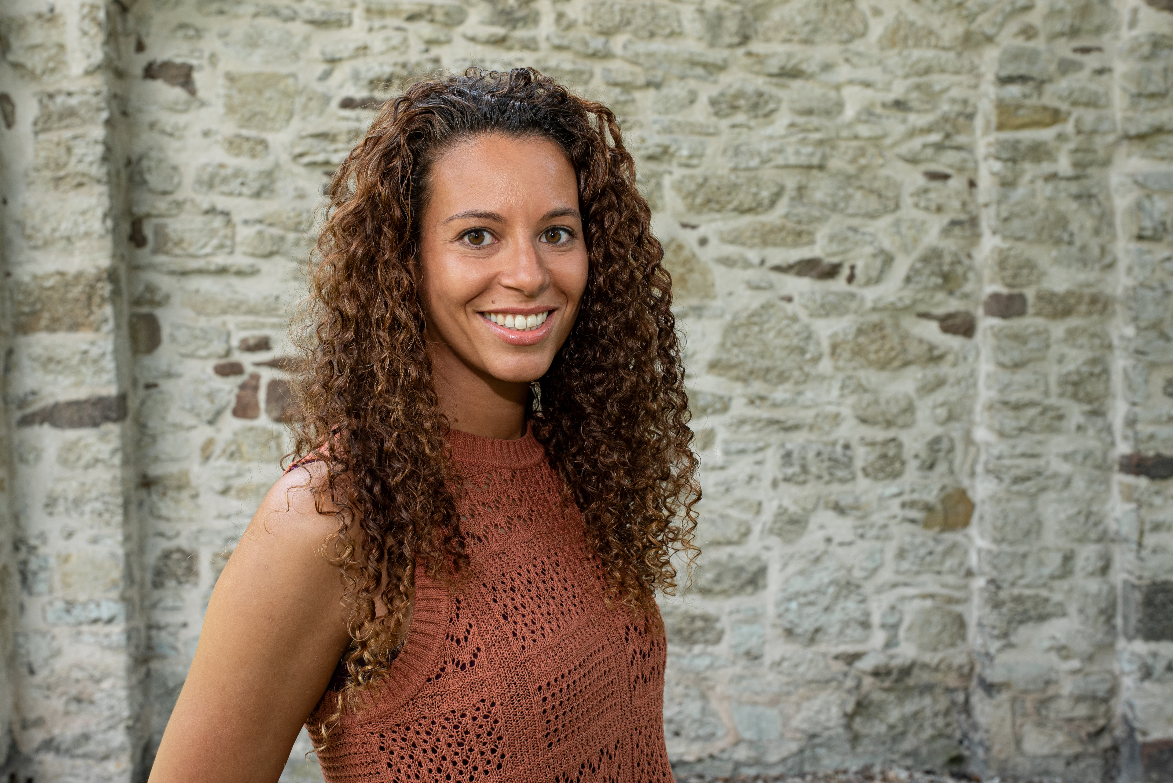 Janina mit lockigen Haaren vor einer Steinmauer