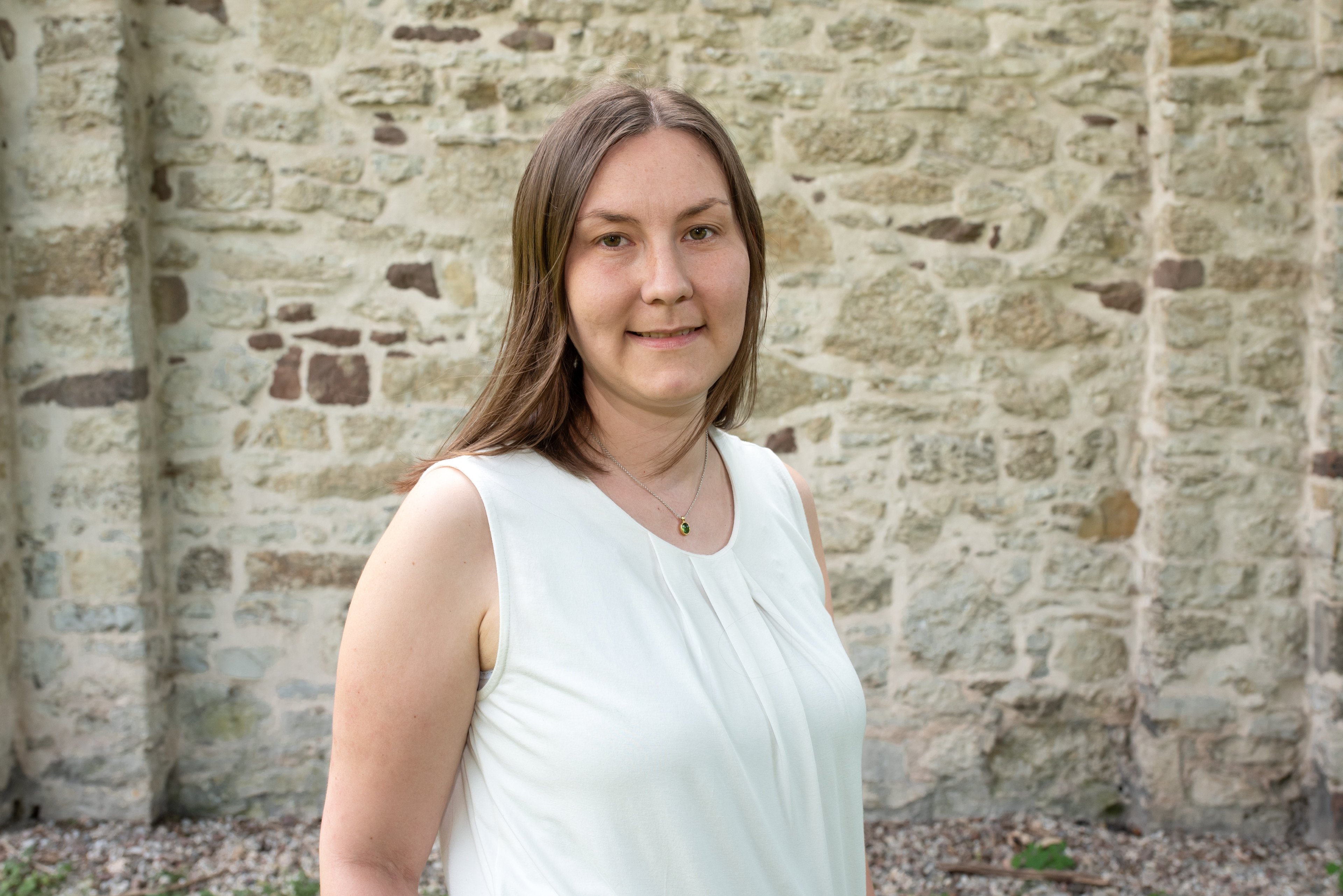 Frau in weißer Bluse vor einer Steinmauer im Freien