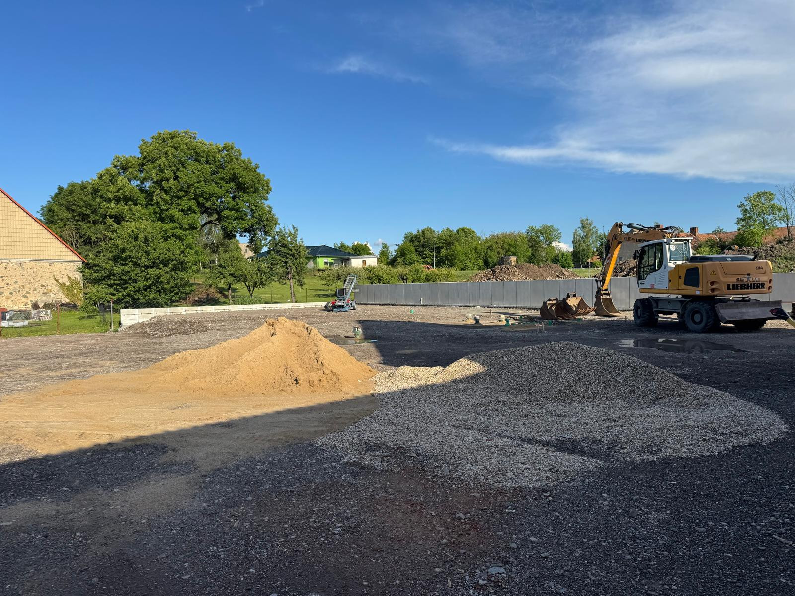 Baustelle mit Bagger, Sand- und Kieshaufen unter blauem Himmel am 22.09.2026