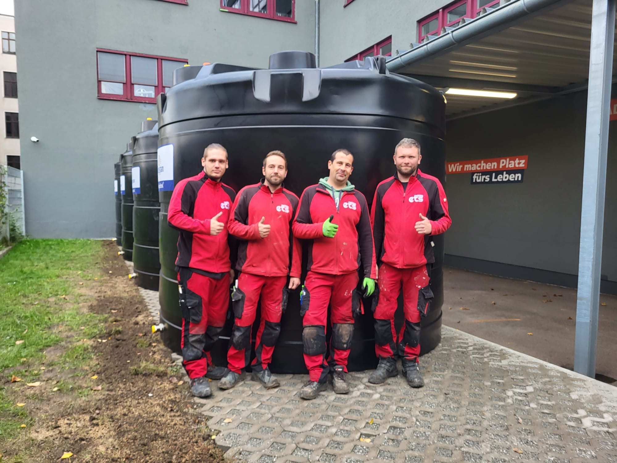 Mitarbeiter der ets vor großen schwarzen Kunststofftanks bei einem Firmengebäude