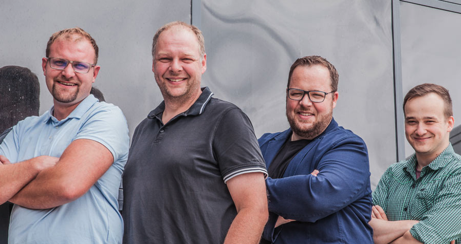 Unsere Ausbilder stehen gemeinsam vor einer Wand und repräsentieren das Ausbildungsteam.