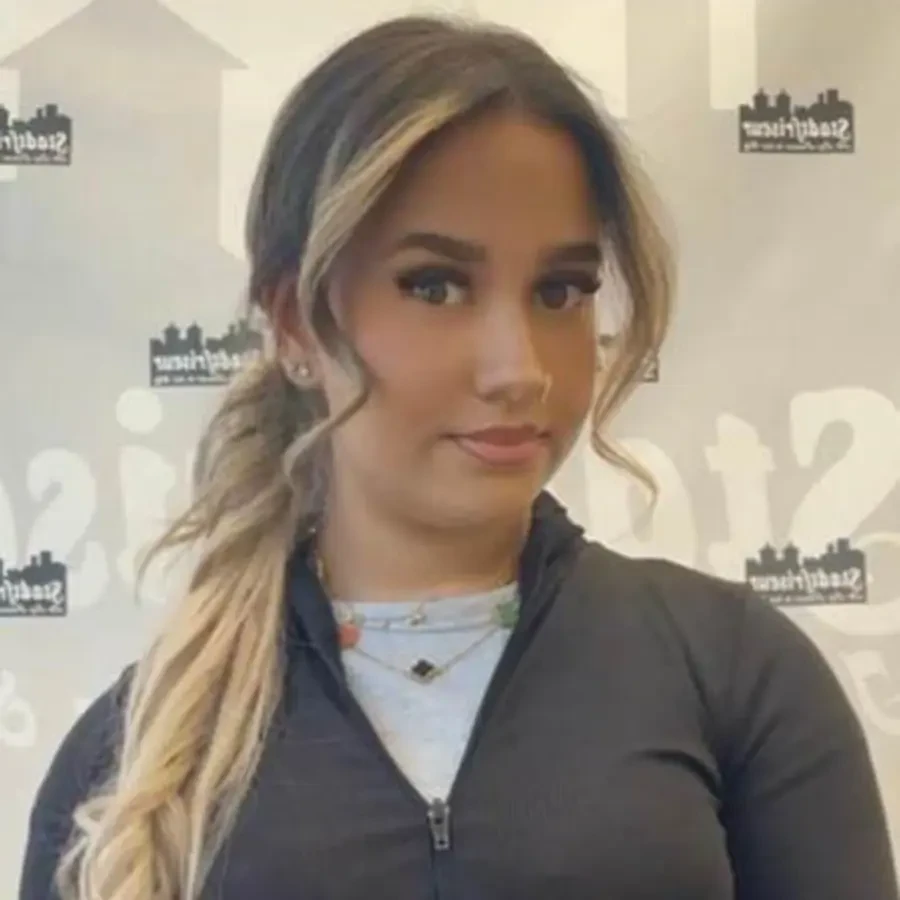 Ilajda vor Hintergrund mit Stadtlogo, Person mit langen Haaren und schwarzer Jacke