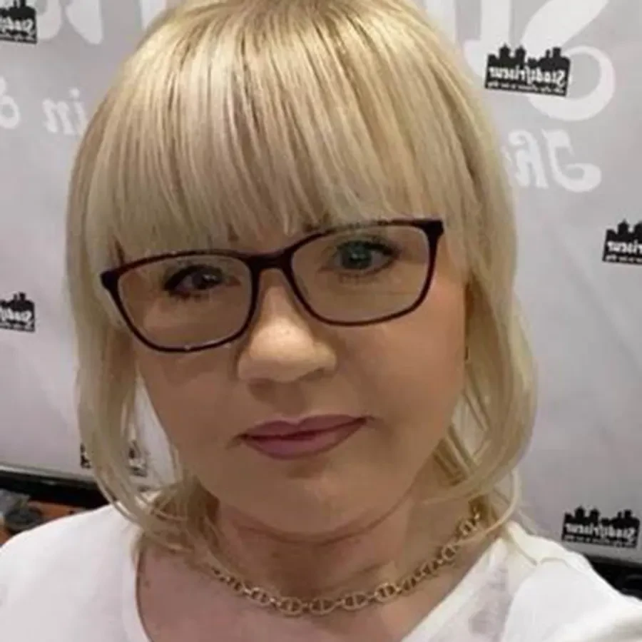 Frau Violetta mit blondem Haar und Kette vor einem Hintergrund mit Schriftzug