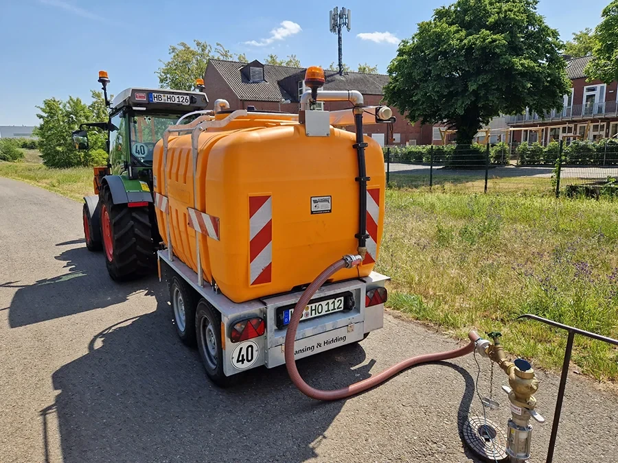 Traktor mit Bewässerungstank bei der Bewässerung einer Grünfläche