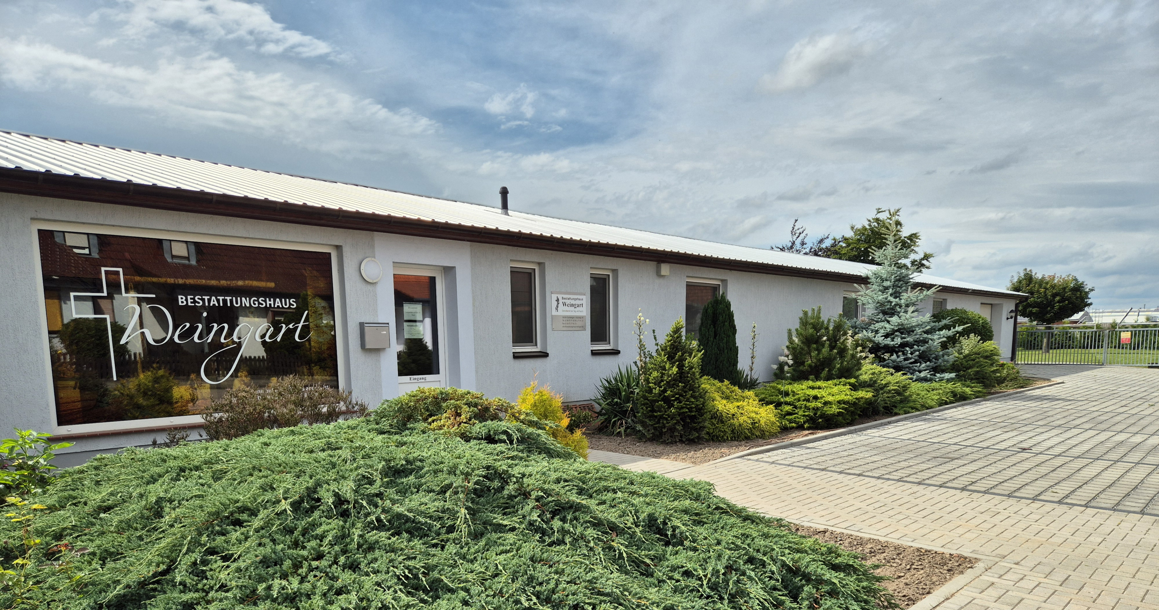 Außenansicht eines modernen Firmengebäudes mit gepflegtem Vorgarten und Firmenschild, aktuelles Foto der Firma