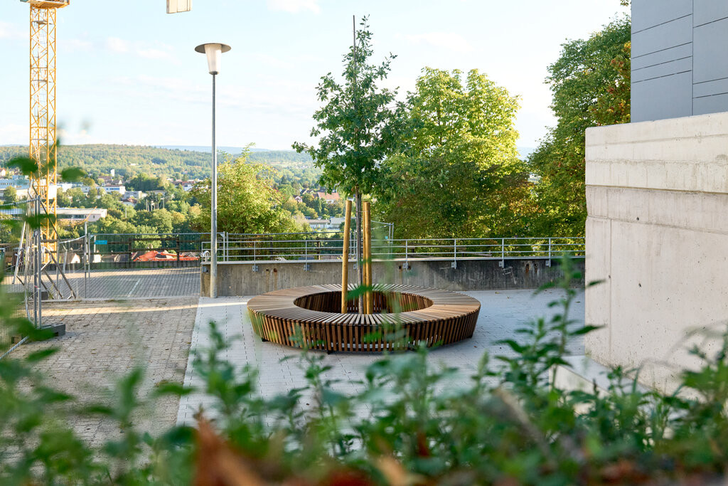 Moderne Sitzbank um Baum auf dem Außengelände von Grüner Daumen Remchingen, aufgenommen am 18.09.2026